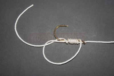 Nous avons ici privilégié le nœud palette 1 pour ce premier hameçon mais d\'autres peuvent être utilisés. Le fil est passé dans l\'œillet et reste accolé à la hampe. L\'essentiel est d\'avoir un fort rejet du brin libre coté courbure afin de pouvoir attacher le second hameçon.  Vous constaterez qu\'ainsi le fil est parfaitement dans l\'alignement de la hampe.