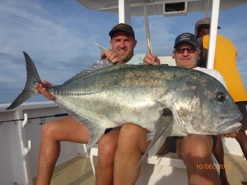 Deux pêcheurs posent fièrement à bord d'un bateau avec une carangue ignobilis massive, un poisson de sport réputé pour sa puissance.